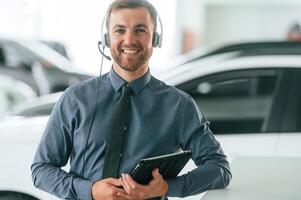 Manager, is, in the headphones and with notepad. Handsome car dealership worker is with electric vehicle photo