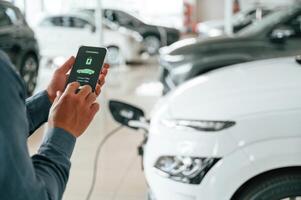 Using smartphone app ,for monitoring charging process. Close up view of man that is with electrical car photo