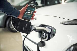 Using smartphone ,app for, monitoring charging process. Close up view of man that is with electrical car photo