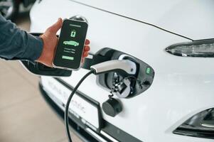 Using smartphone app for, monitoring charging process. Close up view of man that is with electrical car photo