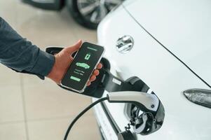 Charging, process on the ,smartphone app. Close up view of man that is with electrical car photo
