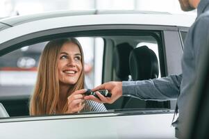 Giving, the keys. Man, in formal clothes is with woman customer with the electric car photo