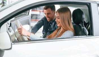 Showing the controls of the automobile, sitting. Man in formal clothes is with woman customer with the electric car photo