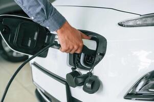 Putting ,charger, into electrical car socket. Close up view of man photo