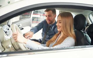 Explaining how automobile works. Man in formal clothes is with woman customer with the electric car photo