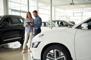 Beautiful ,white automobile. Man ,in formal clothes is with woman customer with the electric car photo