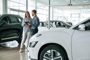 Beautiful white automobile. Man, in, formal clothes is with woman customer with the electric car photo