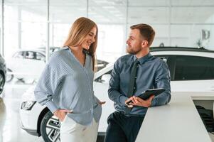 Information in the notepad. Man in ,formal clothes is with woman customer with the electric car photo
