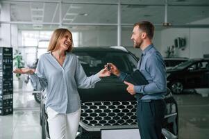 Buying the automobile, taking keys. Man, in formal clothes is with woman customer with the electric car photo