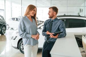 Information, in the notepad. .Man in formal clothes is with woman customer with the electric car photo