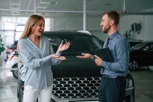 Buying the automobile,, taking keys.. Man in formal clothes is with woman customer with the electric car photo