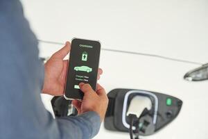 Charging, process on the smartphone app. Close up view of man that is with electrical car photo