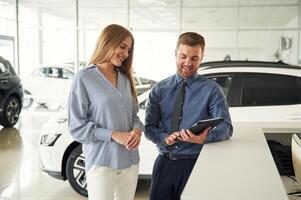 Information ,in the ,notepad. Man in formal clothes is with woman customer with the electric car photo