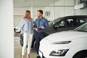 Choosing, the automobile. Man ,in formal clothes is with woman customer with the electric car photo