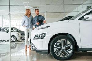Choosing, the, automobile. Man in formal clothes is with woman customer with the electric car photo