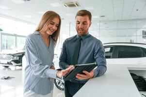 Information, in the notepad. Man in formal clothes is with woman customer with the electric car photo