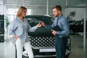 Buying ,the, automobile, taking keys. Man in formal clothes is with woman customer with the electric car photo