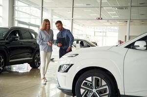 Man, in formal clothes is with woman customer with the electric car photo