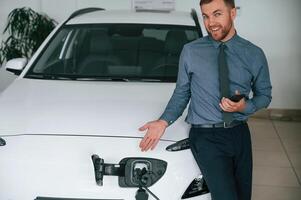 Showing,, the charging process. Handsome car dealership worker is with electric vehicle photo