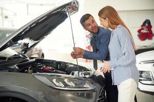 Under ,the hood. Man in formal clothes is with woman customer with the electric car photo