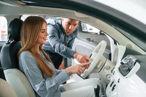 Explaining ,how ,automobile ,works. Man in formal clothes is with woman customer with the electric car photo