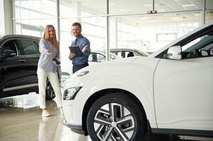 Beautiful, white automobile. Man in formal clothes is with woman customer with the electric car photo