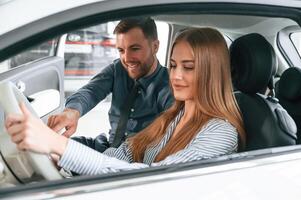 Showing ,the controls of the automobile, sitting. Man in formal clothes is with woman customer with the electric car photo
