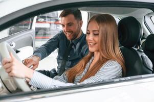Showing the ,controls of the automobile, sitting. Man in formal clothes is with woman customer with the electric car photo