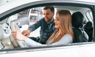 Explaining ,how,automobile works. Man in formal clothes is with woman customer with the electric car photo