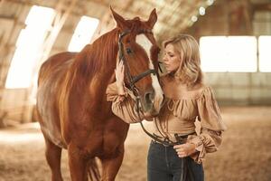 Embracing the head of the animal. Beautiful young woman is with horse indoors photo