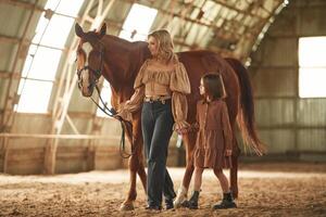 Woman, with ,her little daughter is with horse indoors photo