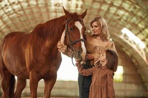 Woman with her little daughter ,is with horse indoors photo