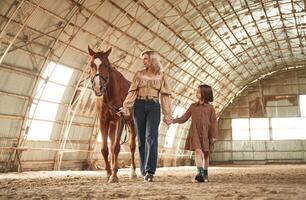 Distant view.. Woman with her little daughter is with horse indoors photo