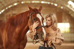 Standing, and, embracing the animal. Beautiful young woman is with horse indoors photo