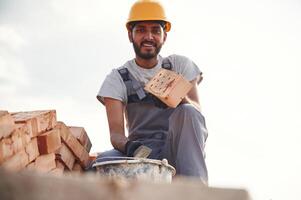 Bucket on ,the, ground, holding a brick. Handsome Indian man is on the construction site photo