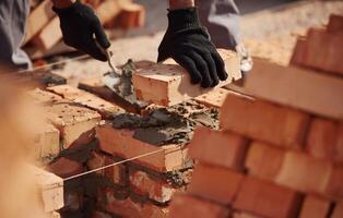 In, gloves, holding brick. Close up view of man that is working on the construction site photo