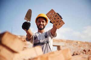 Showing and holding little ,shovel ,and brick. Handsome Indian man is on the construction site photo