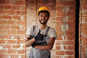 Indoors, against ,brick wall. Handsome Indian man is on the construction site photo