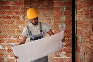 Big paper with plan of the building on it. Handsome Indian man is on the construction site photo