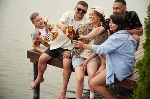 Group of friends are, sitting ,near the lake with beer in hands photo