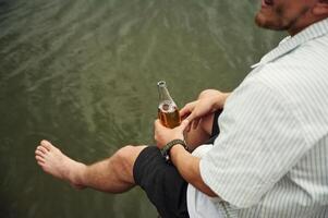 Close, up, view of man that is sitting by the water with beer in hands photo