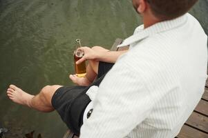 Close ,up view of man that is sitting by the water with beer in hands photo