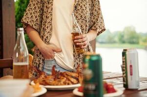 Close up view of woman that is standing by table that is with food, holding beer bottle photo