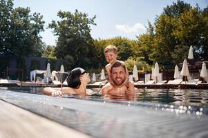 Boy is sitting on, man shoulders. .Happy family of father, mother and son are in the pool photo