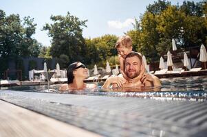 Boy is sitting on man ,shoulders. Happy family of father, mother and son are in the pool photo