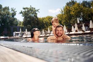 Boy is sitting ,on man shoulders. Happy family of father, mother and son are in the pool photo
