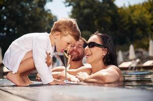 Boy is tasting the lime. Happy family of father, mother and son are in the pool photo