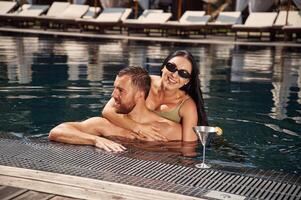 Embracing each other. Man with woman is in the pool together photo