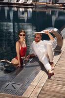 With ,newspaper in hand. Man ,with woman is in the pool together photo