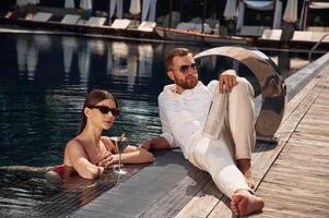 With newspaper in, hand. Man with woman ,is in the pool together photo